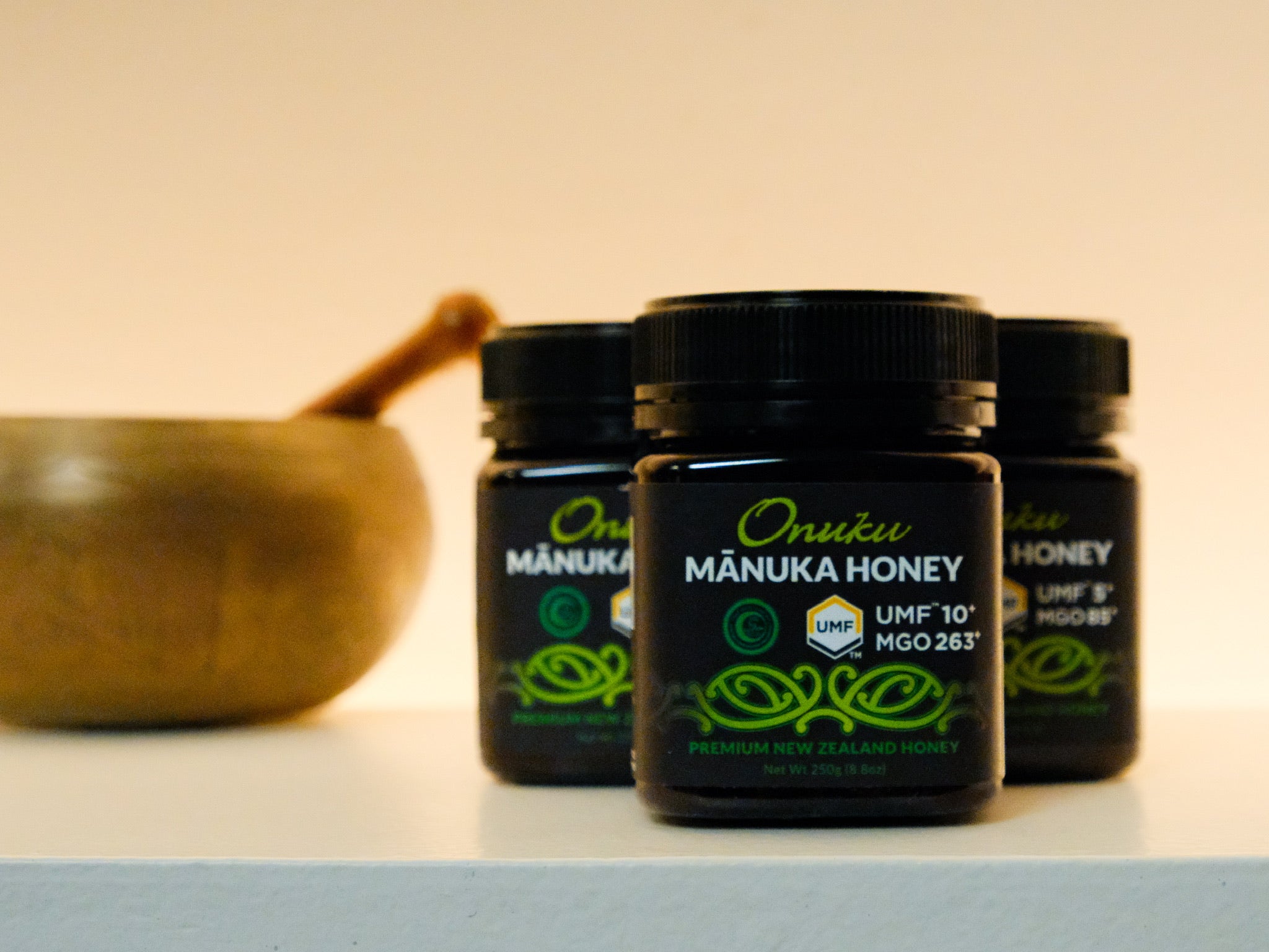 Three jars of Oniku Manuka Honey on a light surface with a blurred background