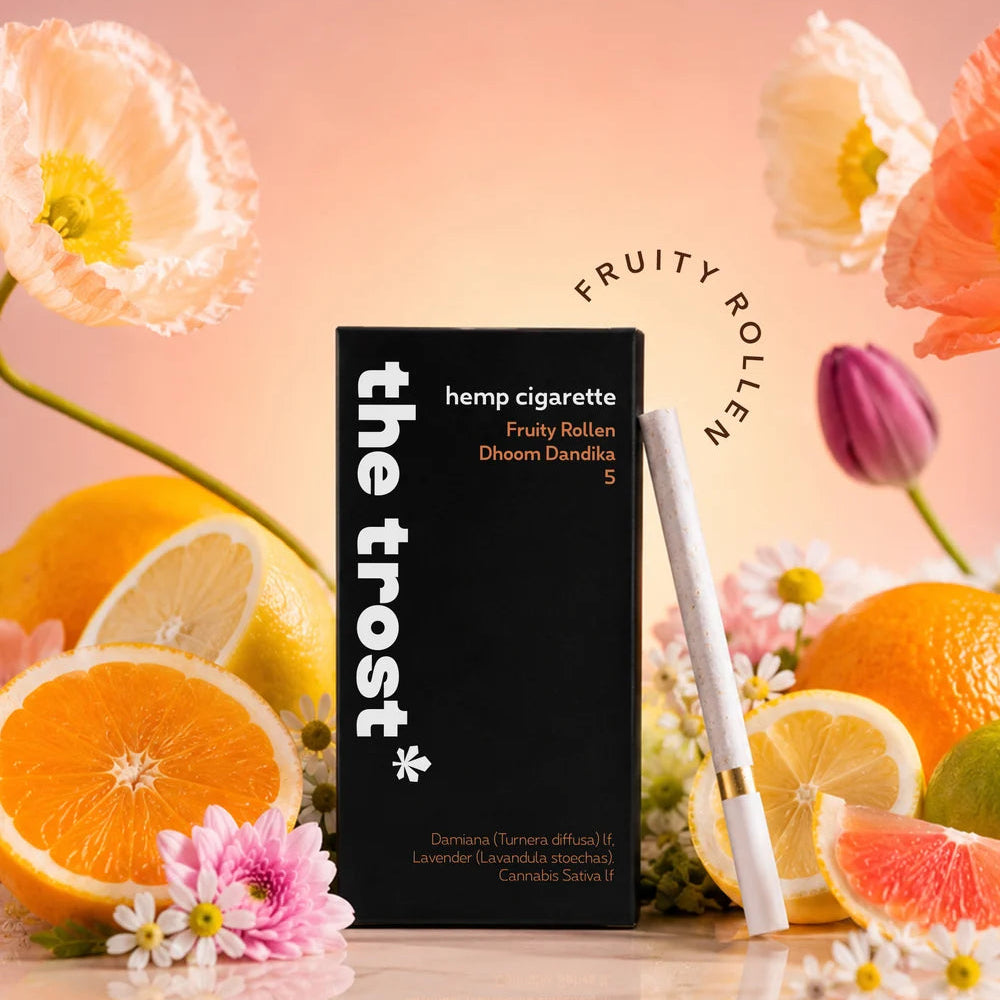 Hemp cigarette packaging with 'the trost' brand name, surrounded by fruits and flowers on a reflective surface.