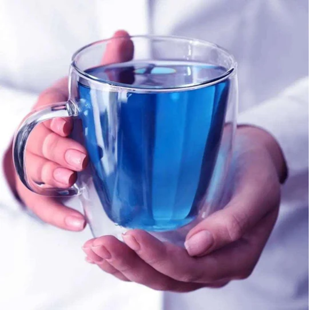 Hands holding a clear mug with blue liquid against a white background