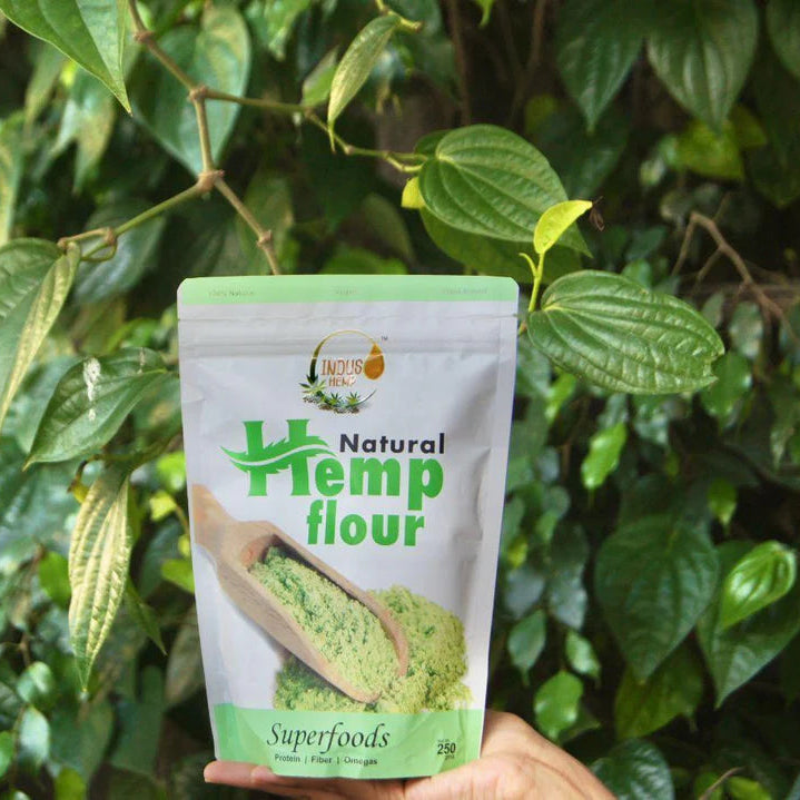 Hand holding a package of 'Natural Hemp flour' against a green leafy background