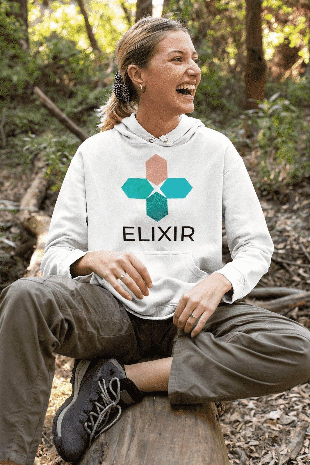 Woman sitting in forest wearing a white hoodie with Elixir brand logo and brown cargo pants
